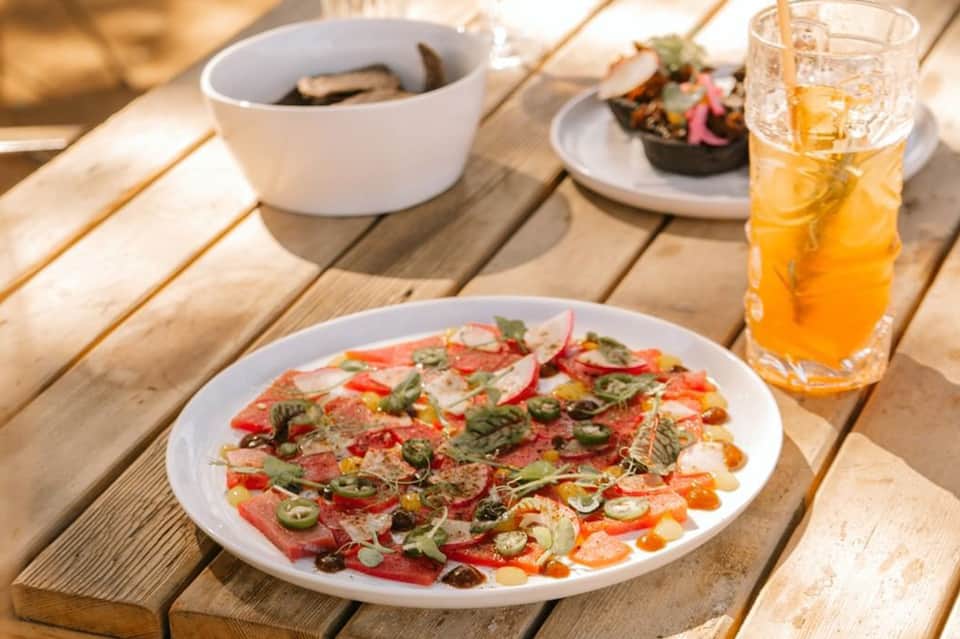 Outdoor dining table with fresh ceviche, soup, and citrus beverage in sunlight
