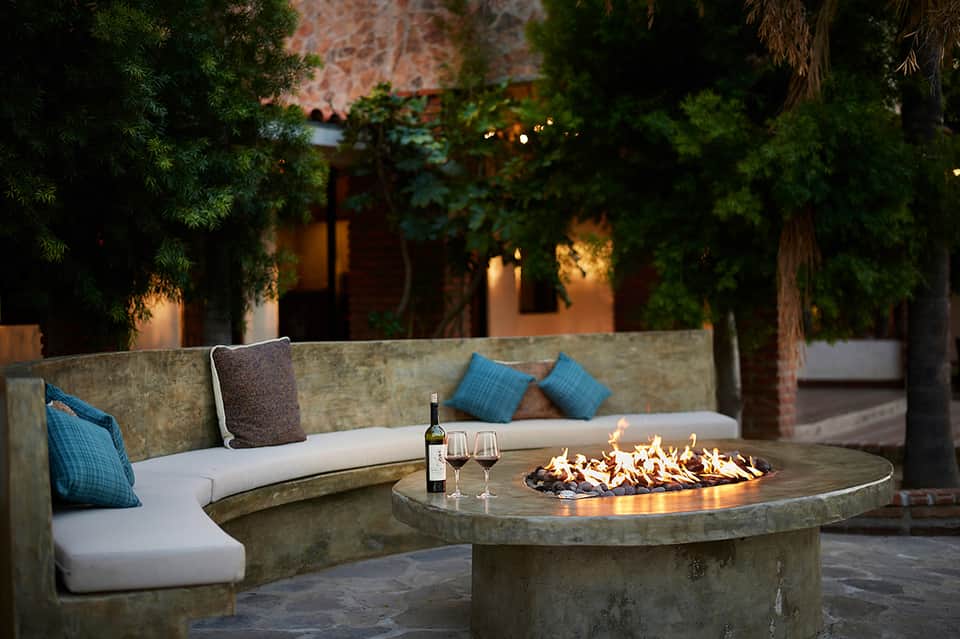 Circular concrete fire pit lounge with built-in seating, wine, and evening garden lighting