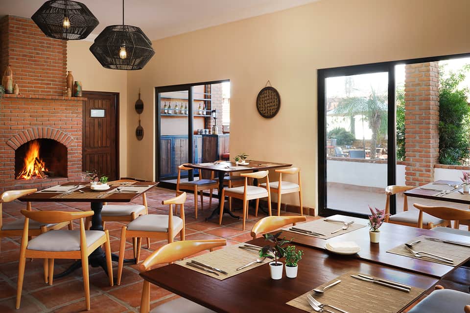 Contemporary restaurant interior with brick fireplace, dining tables, wood accents, and patio access