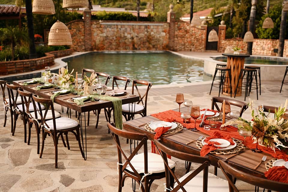 Outdoor dining tables by resort pool with hanging pendant lights and stone walls
