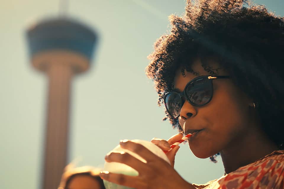 Woman with sunglasses eating while water tower blurs in background, daytime travel shot