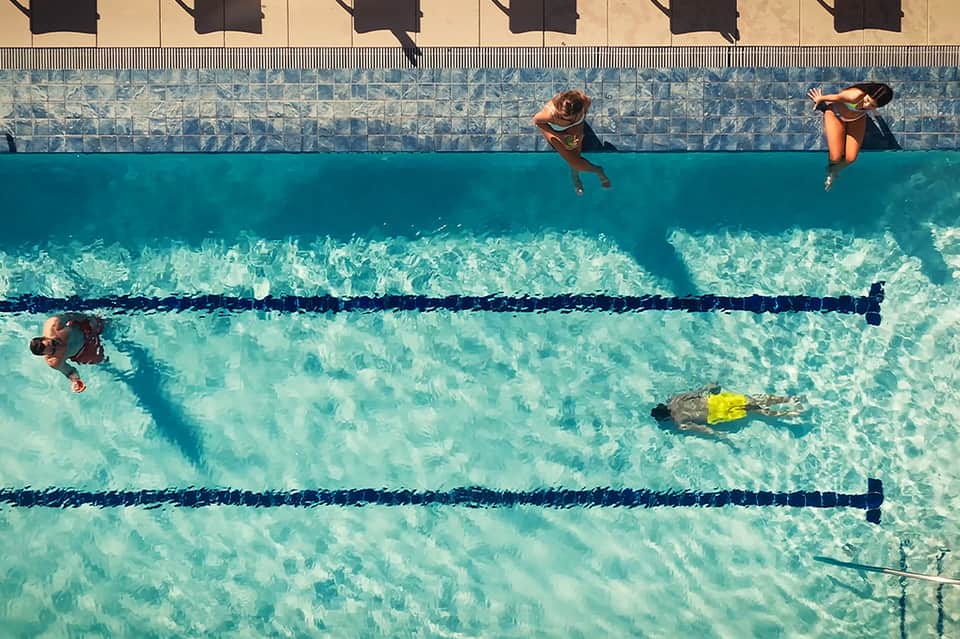 Overhead view of swimmers in lap pool with lane dividers and clearly visible water