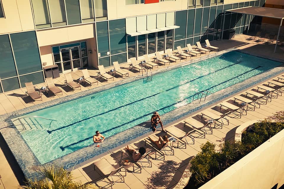 Lap pool with swimmers and lounge chairs along a modern hotel building
