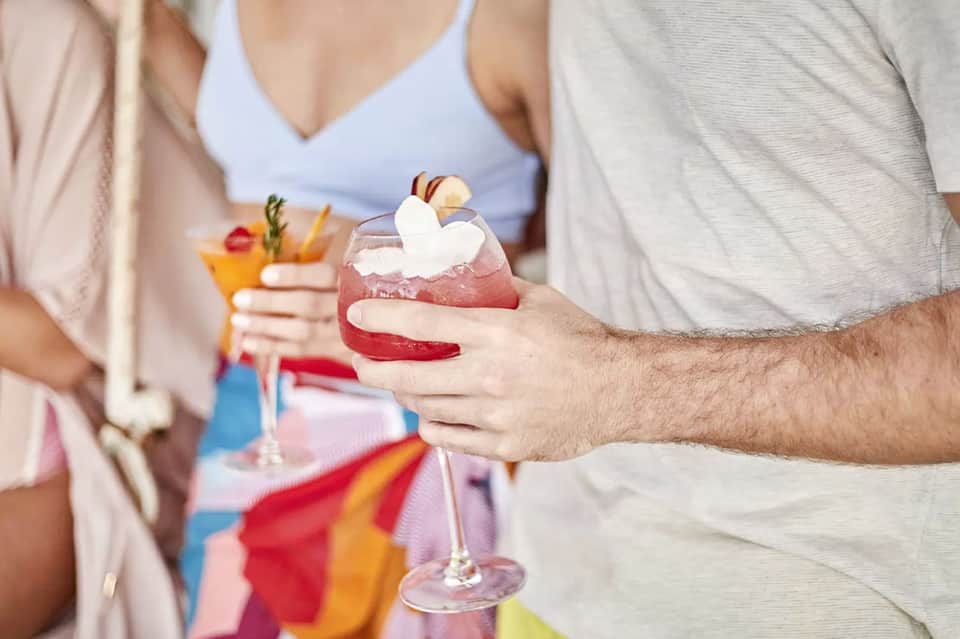 Couple holding tropical cocktails with whipped cream and fruit garnishes at beachside bar