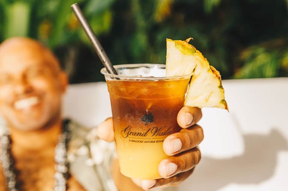 Tropical cocktail with pineapple garnish being held at a resort, green foliage in background