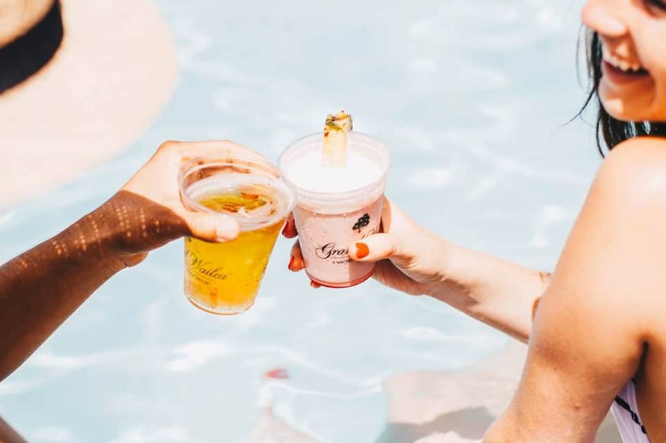 Two people toasting with beer and cocktail while relaxing in resort pool with ocean view