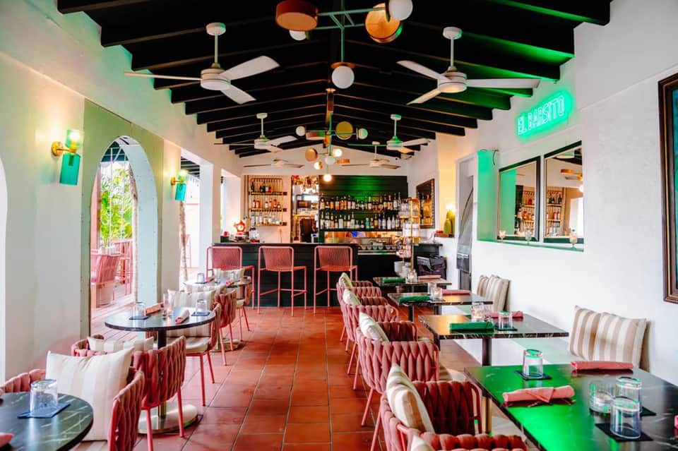 Modern restaurant interior with colorful ceiling details, bar, dining tables, and neon signage