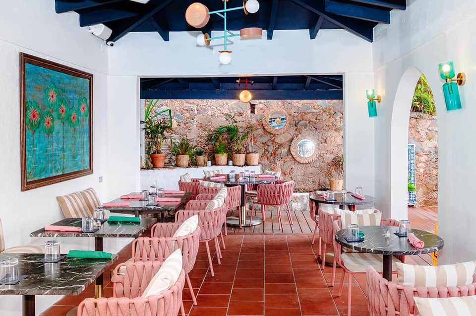 Colorful outdoor restaurant with pink chairs, cork walls, and Mediterranean architectural details