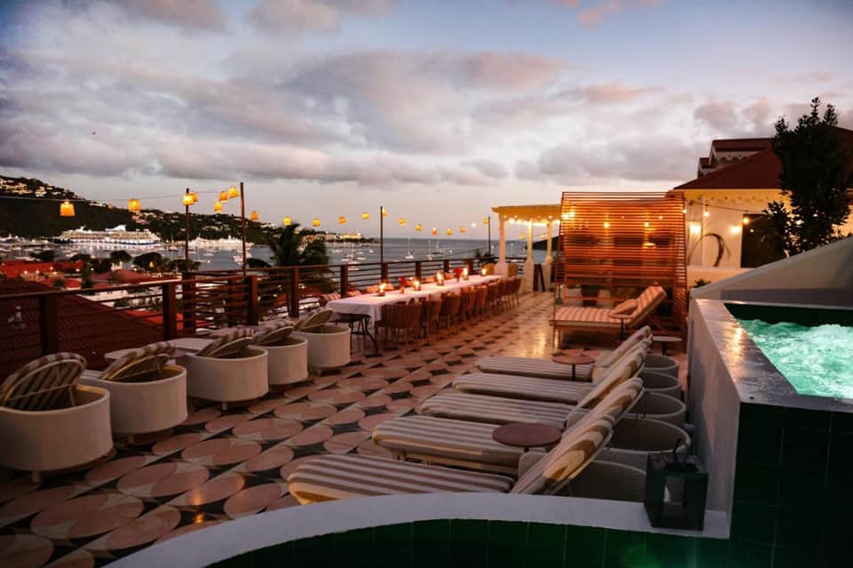 Elegant rooftop terrace at dusk with long dining table, lounge seating, and glowing lantern lighting