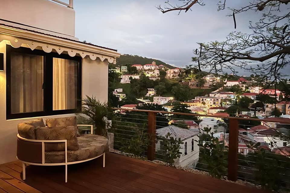 Resort balcony with modern seating overlooking hillside town with red-roofed buildings and tropical vegetation
