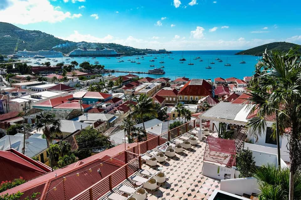 Coastal village with red-roofed buildings, palm trees, turquoise bay, and cruise ship