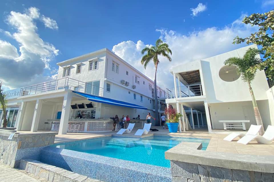 Contemporary white resort building with turquoise pool, modern architecture, palm trees, and blue sky