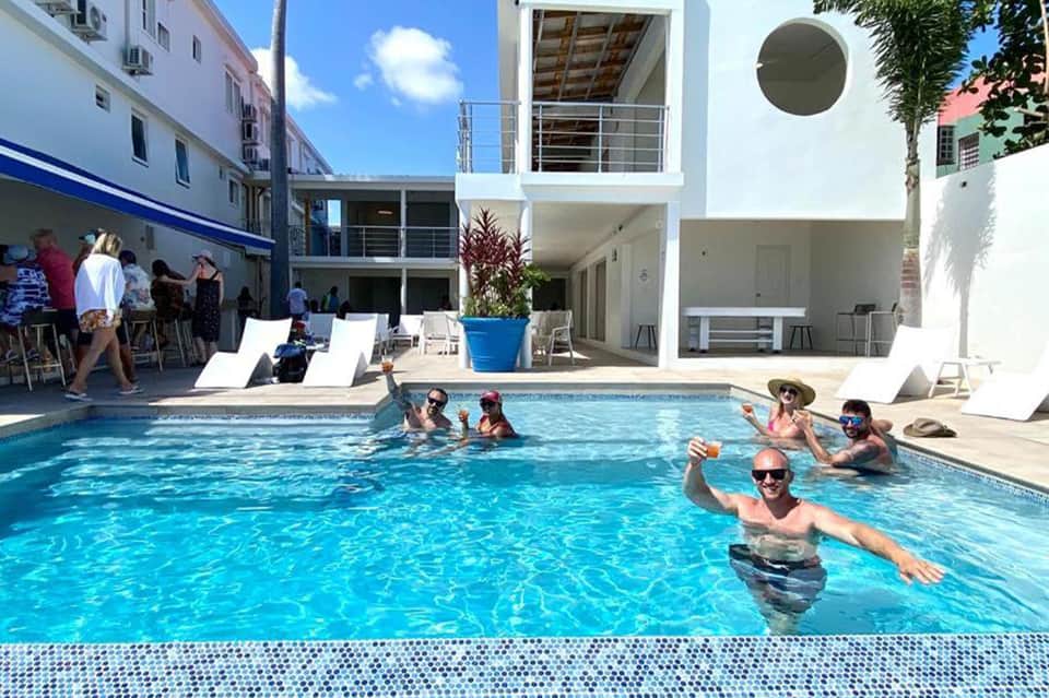 Modern hotel pool with guests swimming, white modernist architecture, and tropical setting