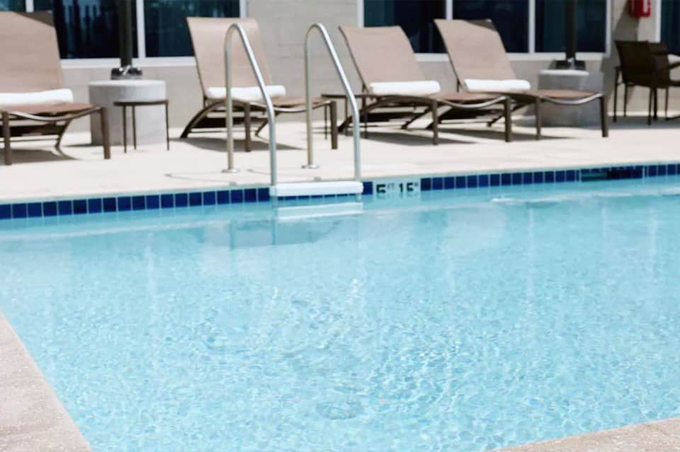 Clean swimming pool with ladder and lounge chairs on concrete deck