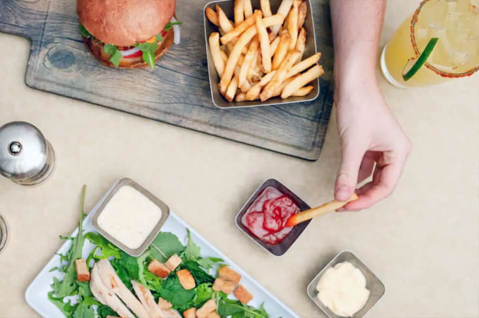 Overhead view of casual meal with burger, fries, salad and beverages on wooden table