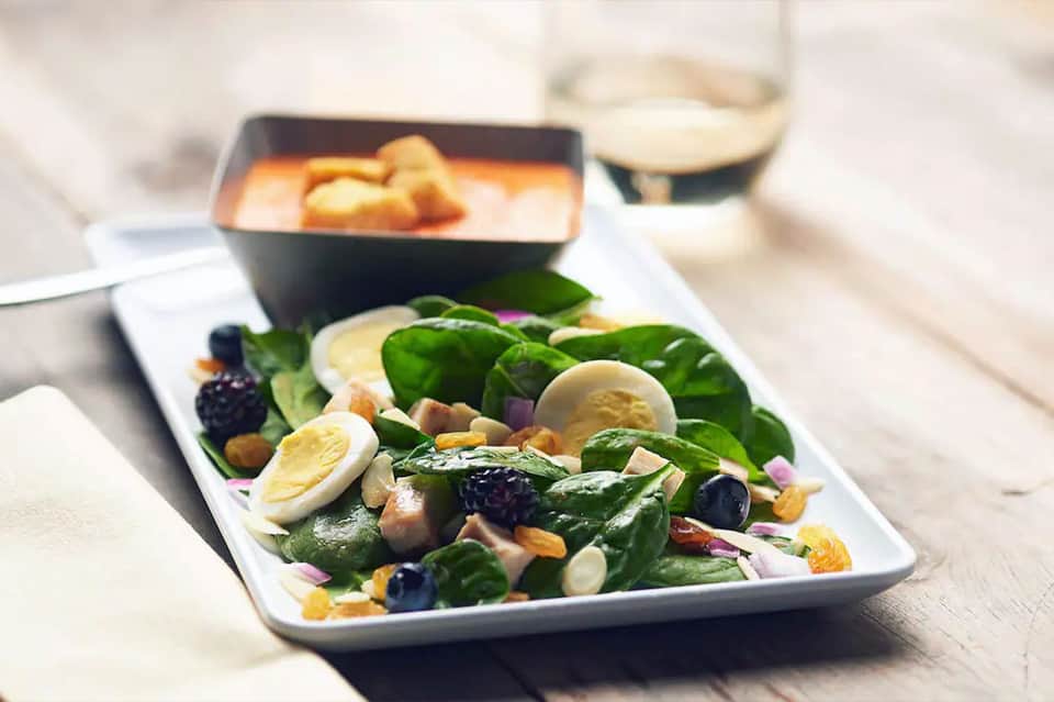 Plated salad with spinach, eggs, and nuts served with soup in black bowl