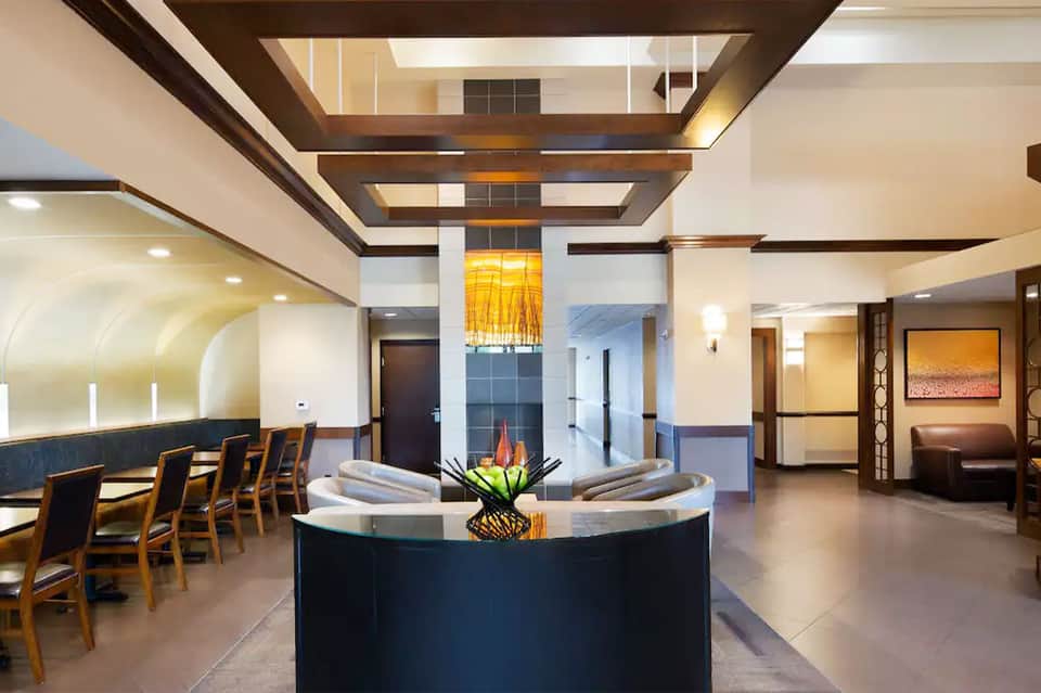 Modern hotel lobby with dark reception desk, wood beams, dining area, and contemporary lighting