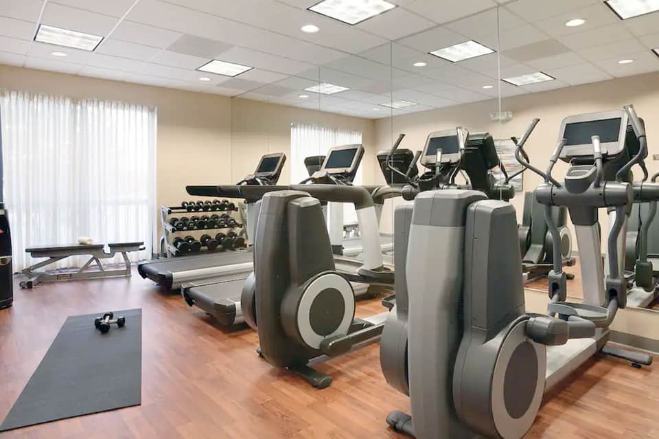 Fitness center with cardio equipment, treadmills, ellipticals, weights, and floor-to-ceiling mirror
