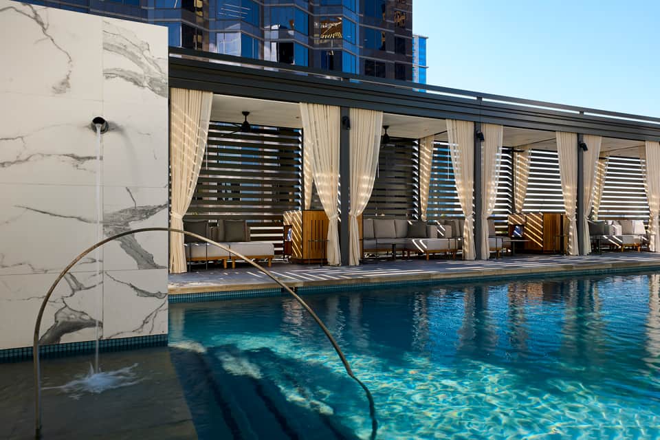 Modern rooftop pool with draped cabanas, marble walls, and city skyline views from urban resort
