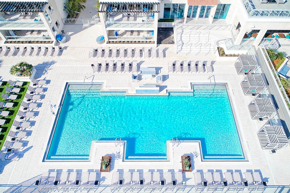 Aerial view of large resort pool with turquoise water, surrounding loungers, and white buildings