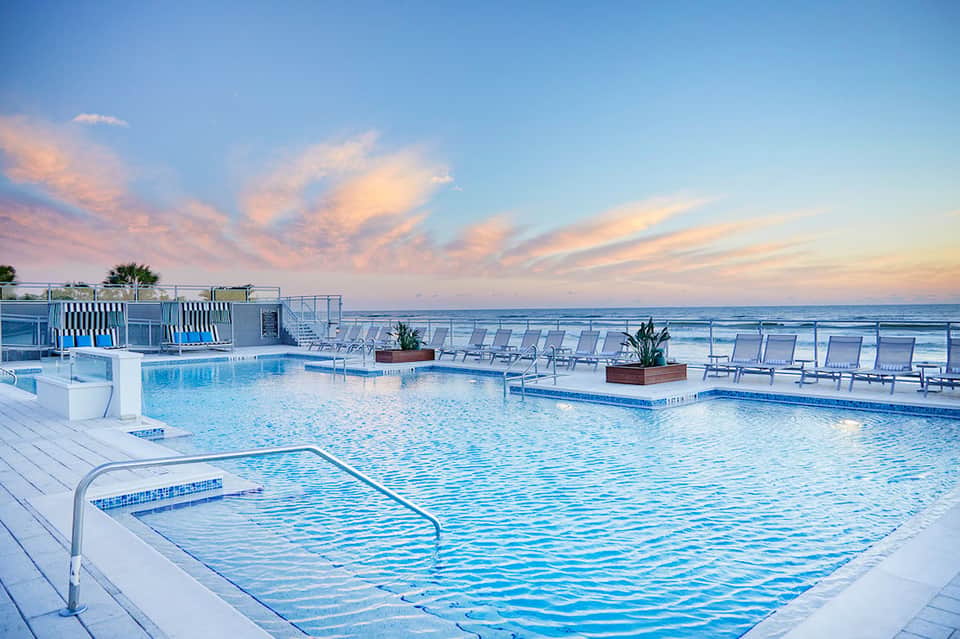 Resort pool deck at sunset with lounge chairs and ocean view at horizon