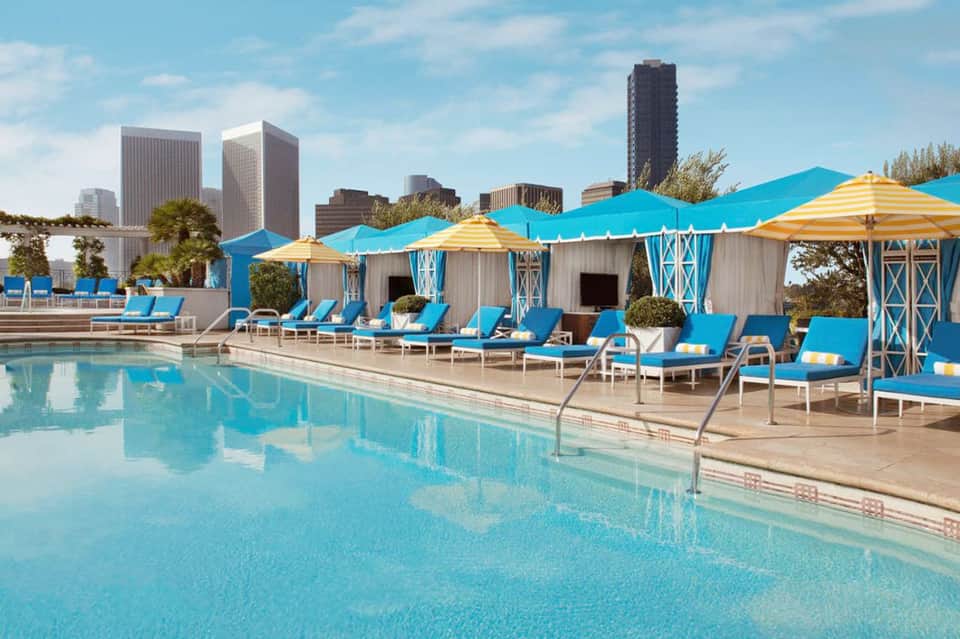 Urban rooftop pool with bright blue cabanas, yellow umbrellas, and city skyline backdrop