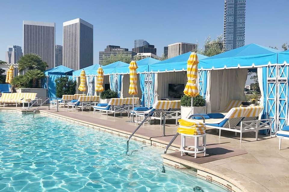 Urban rooftop pool with bright blue tent canopy, yellow umbrellas, and city skyline background