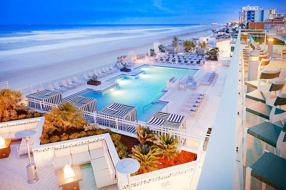 Beachfront resort pool deck at dusk with ocean view and lounge chairs