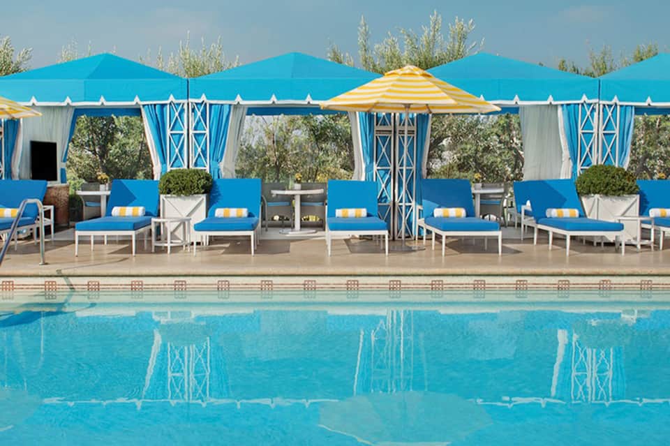 Resort pool with blue and yellow cabanas, lounge chairs, and tent-style seating structures