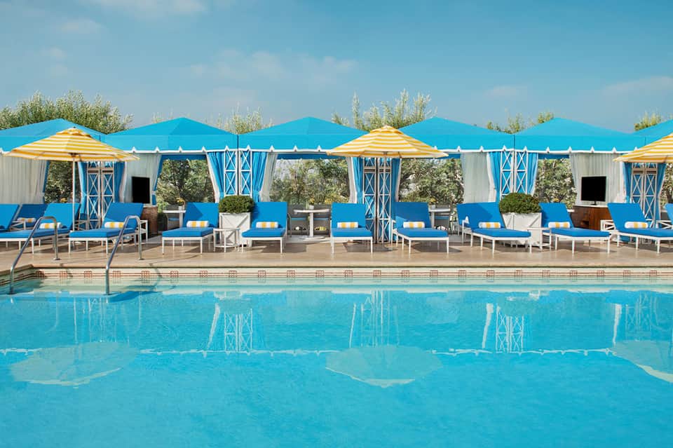 Resort pool with blue and yellow cabanas, striped umbrellas, and manicured landscaping