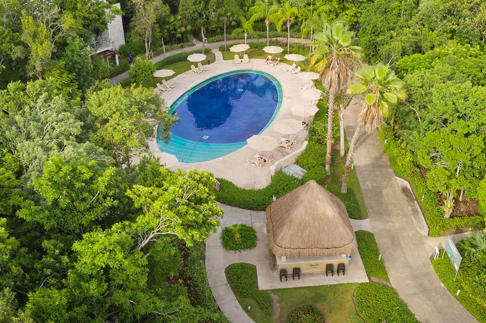 Aerial view of oval pool surrounded by tropical greenery and beach umbrellas