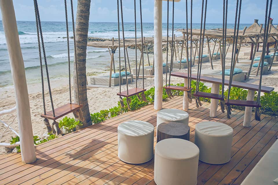 Wooden deck with rope swings over white beach and turquoise ocean