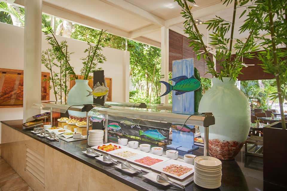 Resort restaurant buffet with chilled display cases, green plant accents, and tropical ambiance