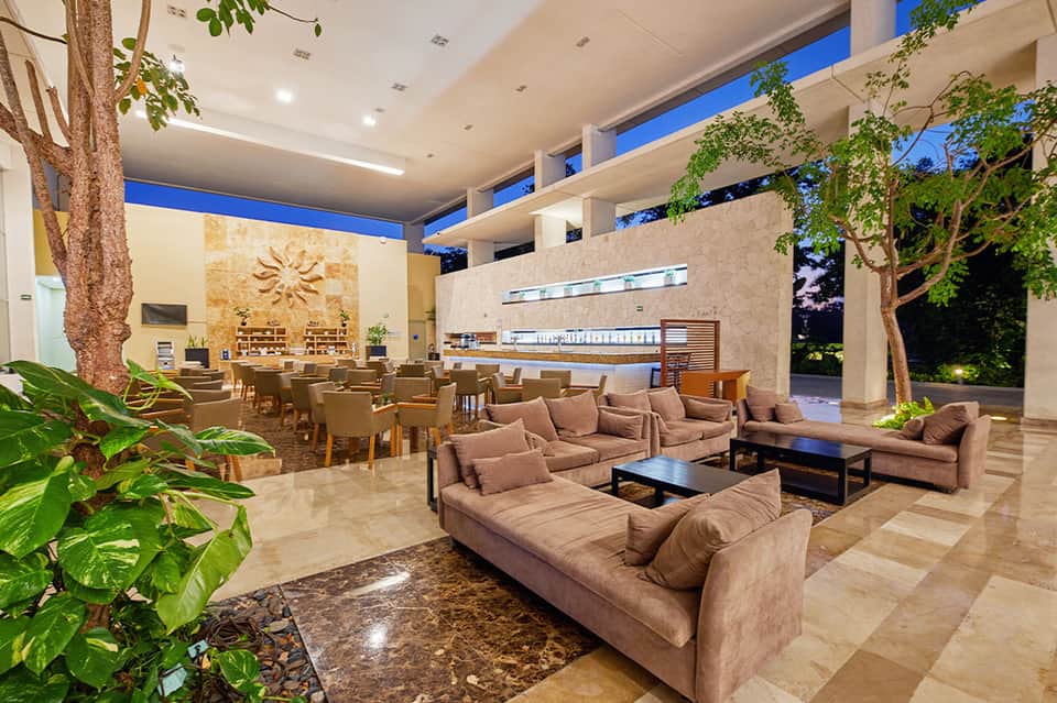 Modern lobby lounge with tall tree, sculptural wall art, reception desk, and open ceiling