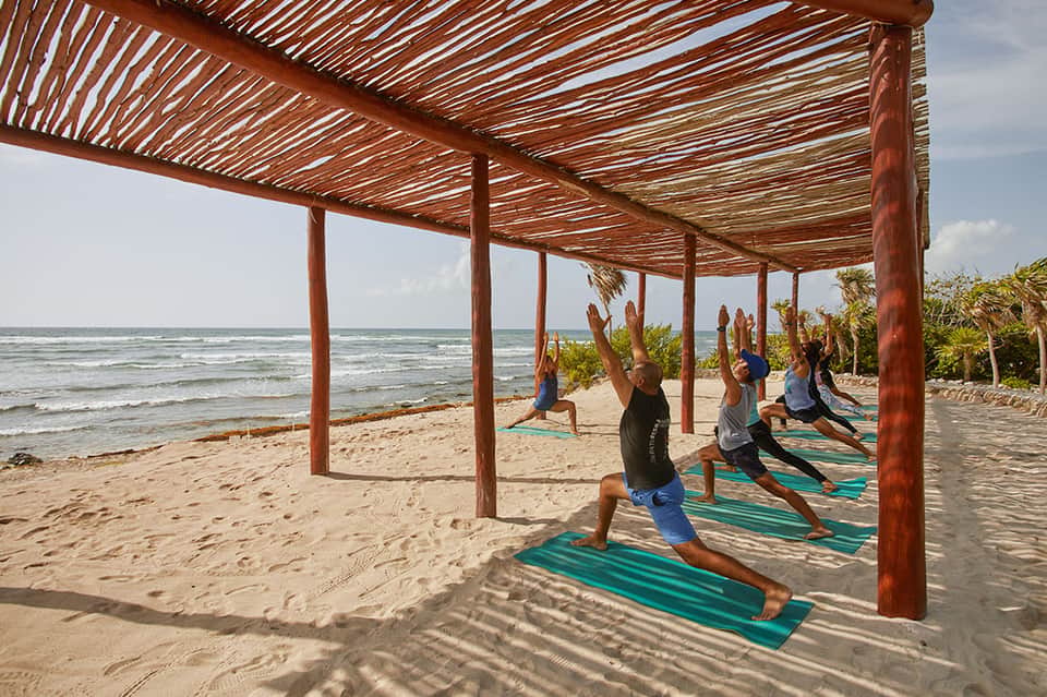 Yoga class on beach under wooden pergola with ocean view