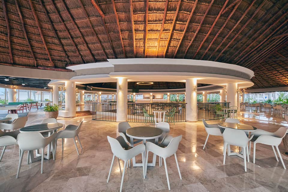 Contemporary resort lounge with thatched ceiling, columns, white seating, and ocean view terrace