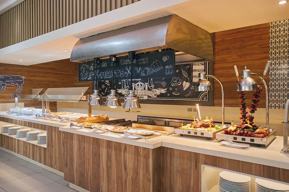 Hotel restaurant buffet counter with carved meat station, charcuterie, and decorative heat lamps