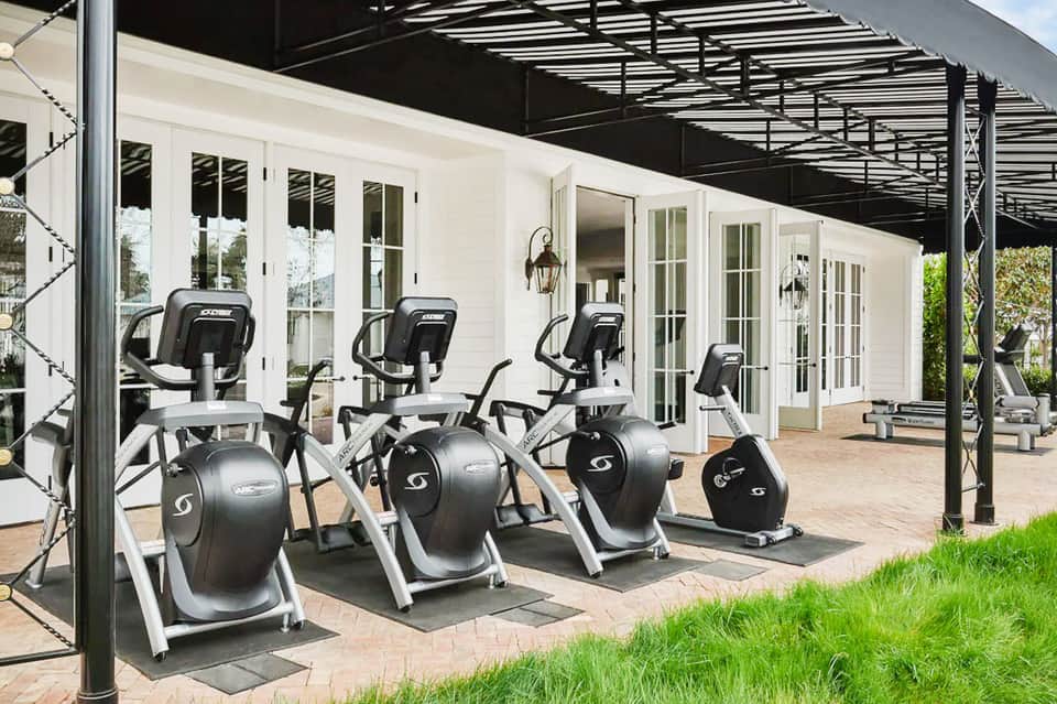 Outdoor fitness area with elliptical machines under pergola near white building