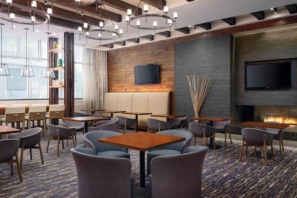 Contemporary hotel lounge with fireplace, pendant lights, wood brick accent wall, and seating areas