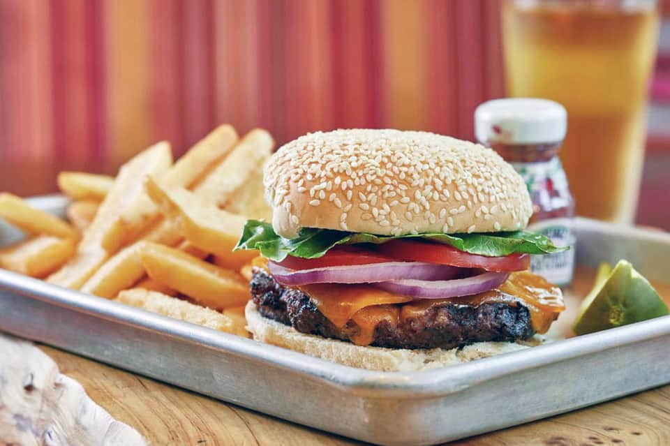 Gourmet burger with fries and beverage on wooden table with red striped background