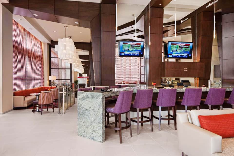 Modern hotel bar and lounge with purple bar stools, wood paneling, and ambient lighting