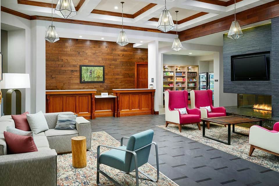 Modern hotel lobby with wood beams, fireplace, colored armchairs, and reception desk