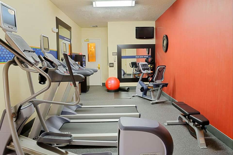 Compact gym with treadmills, elliptical, exercise ball, and orange accent wall