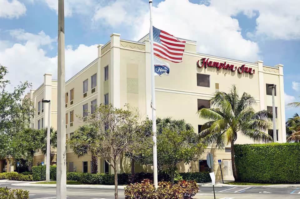 Hampton Inn hotel exterior with American flag and tropical landscaping