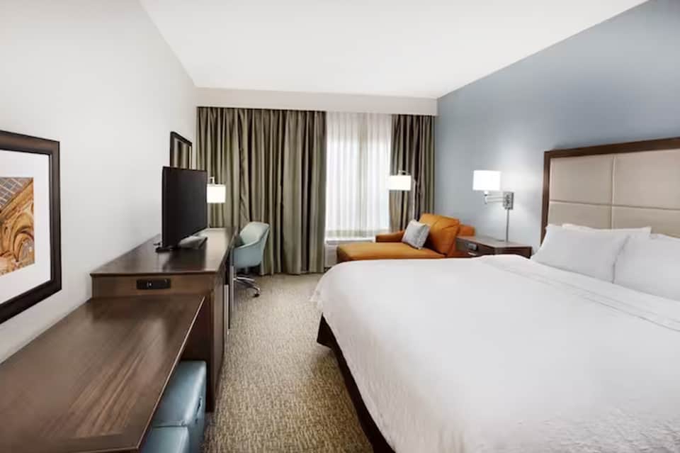 Modern hotel bedroom with queen bed, TV, desk, and contemporary furnishings