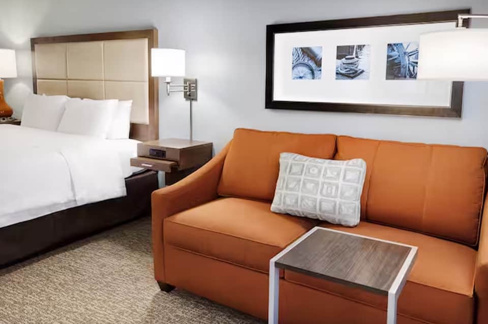 Modern hotel room with cream headboard, orange sofa, and framed coastal photography