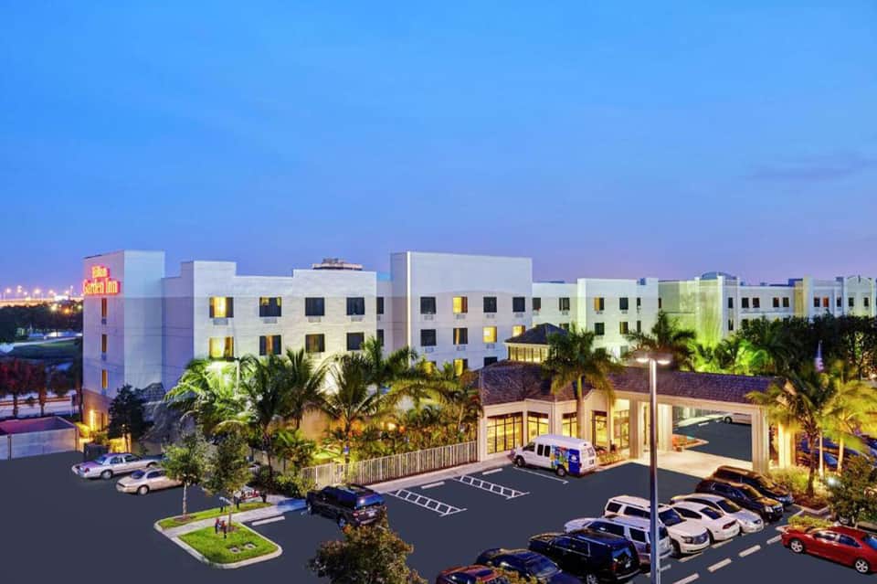 Modern hotel exterior at dusk with illuminated parking area and tropical landscaping