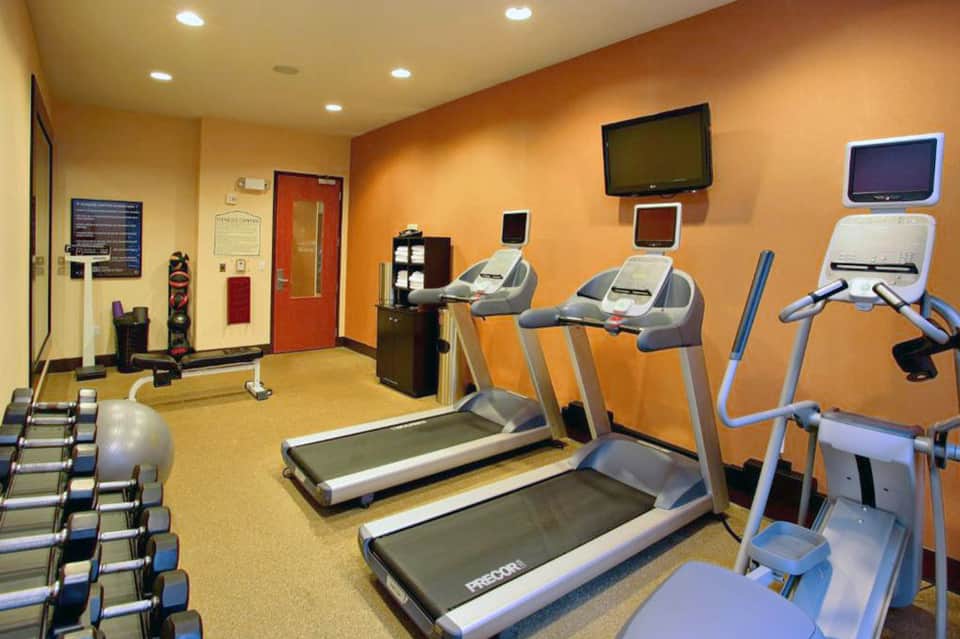 Hotel fitness center with treadmills, exercise equipment, and orange accent walls