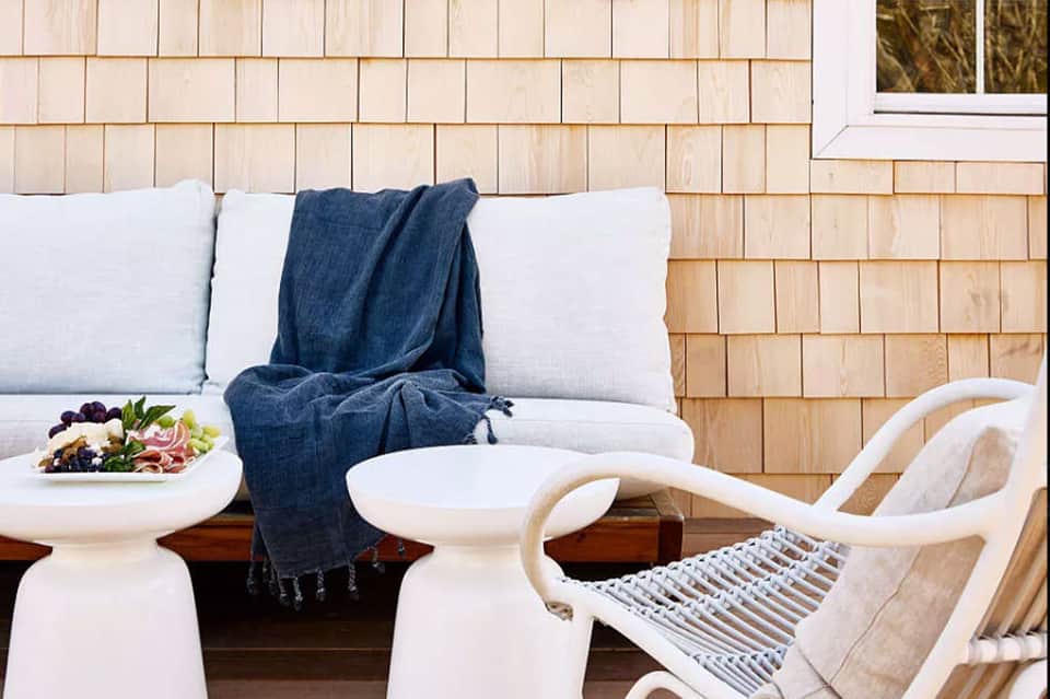 Coastal patio with white furniture, blue throw blanket, and wooden shingle exterior