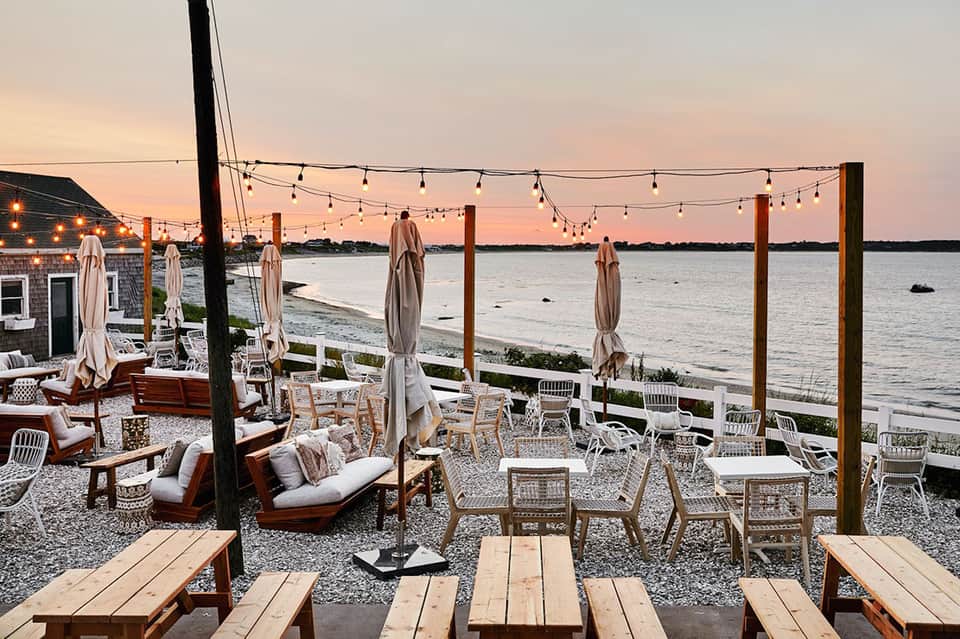 Waterfront patio at dusk with string lights, umbrellas, and sunset views